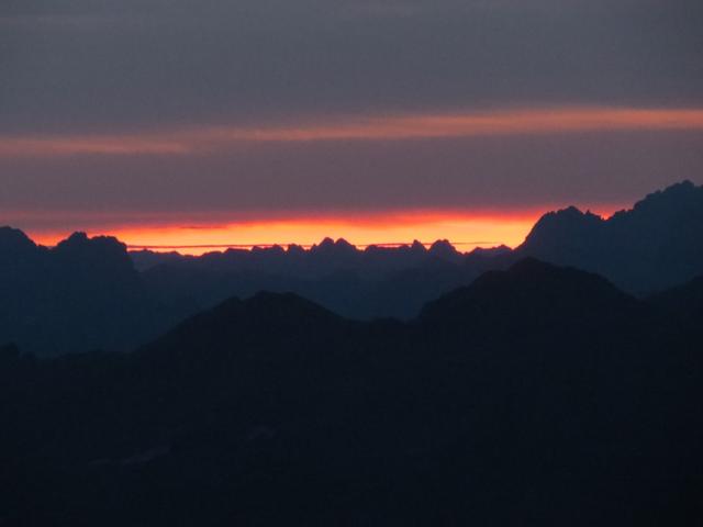 glühend rot taucht die Sonne hinter den Bergen hervor