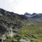 über die Wiese mit einigen Felsblöcken führt der Weg auf die Rippe zu, auf der hoch droben die Hütte zu sehen ist